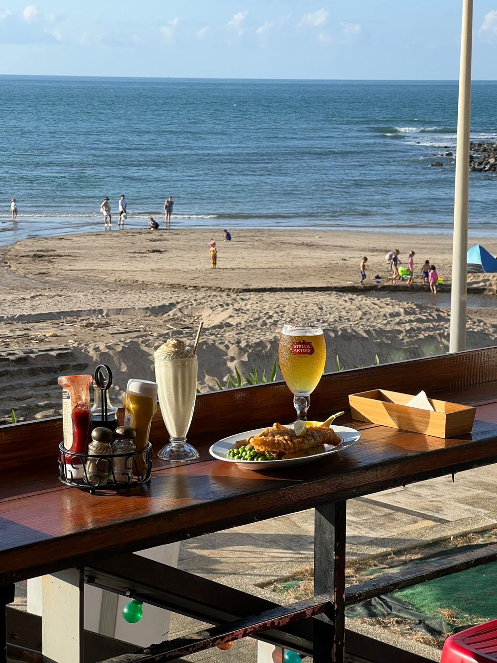 Almoço à beira-mar: peixe com batata frita, milkshake e cerveja numa mesa de frente para a praia